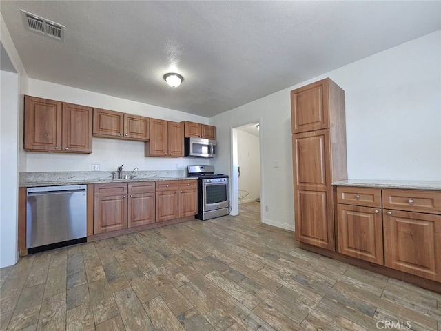 1412 S White Ave, Pomona, CA 91766 - kitchen featuring light wood-style floors, brown cabinetry, stainless steel appliances, and visible vents