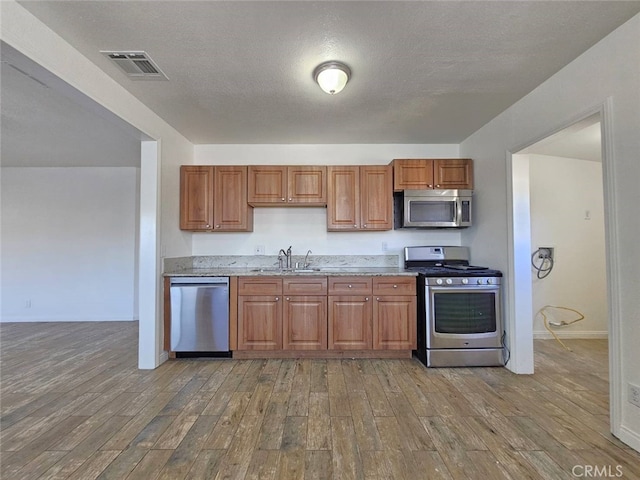 1412 S White Ave, Pomona, CA 91766 - kitchen featuring brown cabinetry, wood finished floors, light stone countertops, a sink, and stainless steel appliances