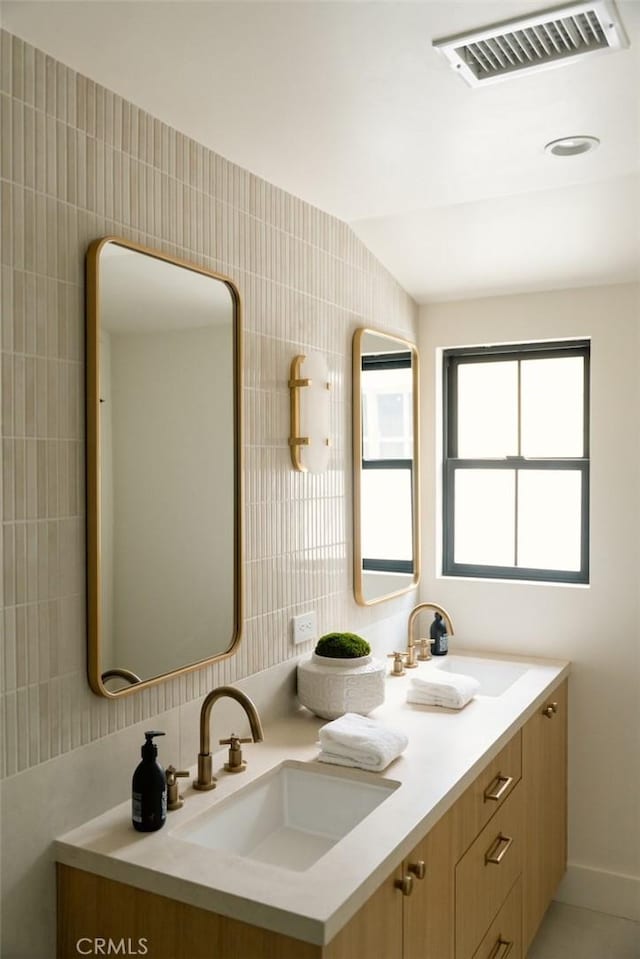 bathroom featuring a sink, tile walls, double vanity, and visible vents