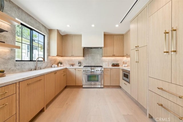 kitchen with stainless steel range, a sink, light wood-style floors, light brown cabinets, and backsplash