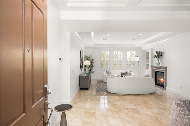 entryway with a glass covered fireplace, a raised ceiling, ornamental molding, and baseboards