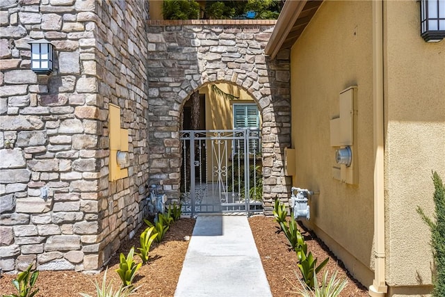 view of exterior entry with a gate, stucco siding, and stone siding