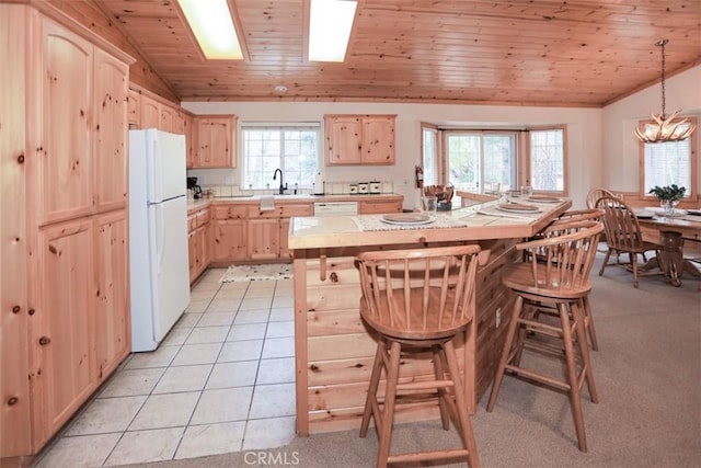 kitchen featuring a kitchen bar, light brown cabinetry, vaulted ceiling, light countertops, and freestanding refrigerator