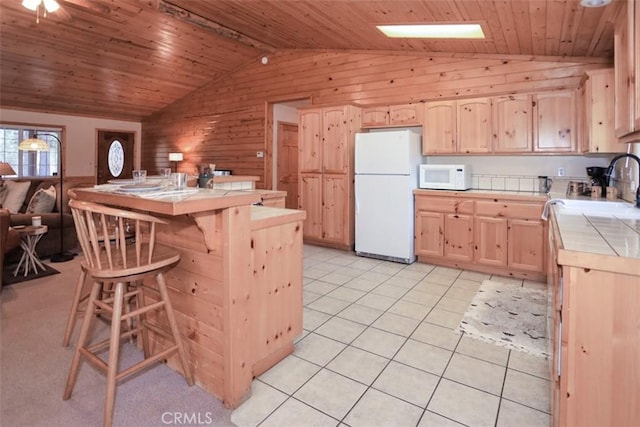 kitchen with light brown cabinets, white appliances, wood walls, tile countertops, and vaulted ceiling with beams