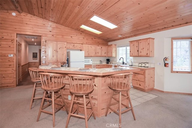 kitchen featuring a breakfast bar area, light brown cabinetry, vaulted ceiling, and white appliances