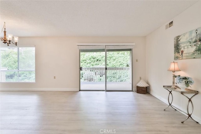 empty room with an inviting chandelier, baseboards, wood finished floors, and a healthy amount of sunlight