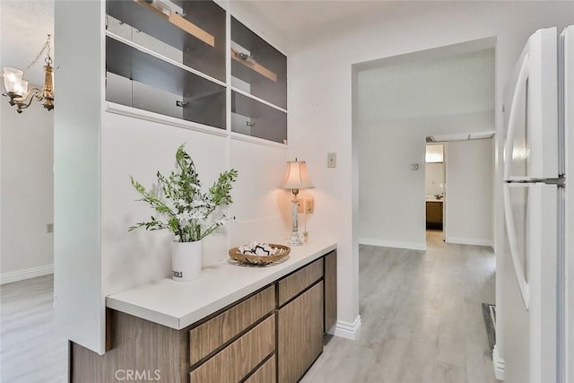 corridor with baseboards, an inviting chandelier, and light wood-style floors