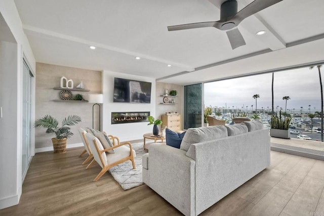 living area with a glass covered fireplace, a ceiling fan, recessed lighting, and wood finished floors