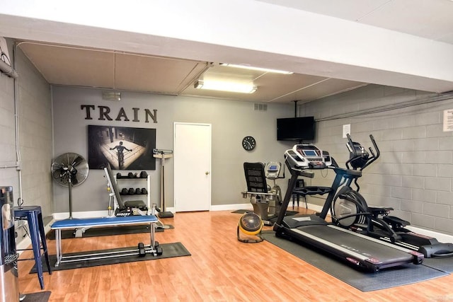 exercise room with concrete block wall, visible vents, and wood finished floors