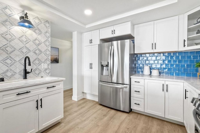 kitchen with white cabinets, stainless steel fridge, a sink, light wood finished floors, and tasteful backsplash