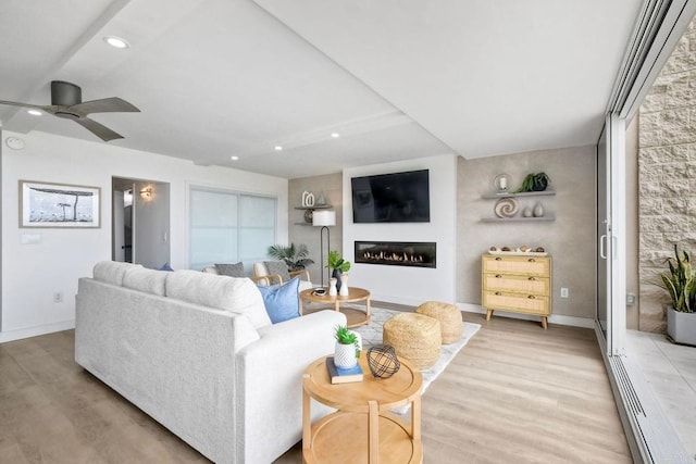 living area featuring ceiling fan, light wood finished floors, a glass covered fireplace, recessed lighting, and baseboards
