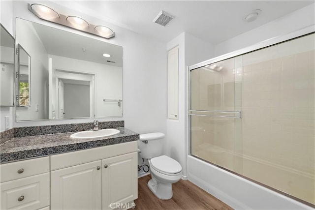 full bath featuring wood finished floors, toilet, vanity, and enclosed tub / shower combo