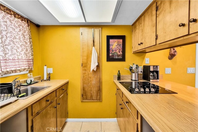 kitchen with baseboards, black electric stovetop, light countertops, a sink, and light tile patterned floors