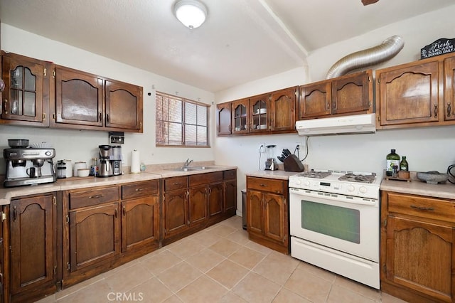 1107 B St, Brawley, CA 92227 - kitchen with white gas stove, light countertops, a sink, under cabinet range hood, and light tile patterned flooring