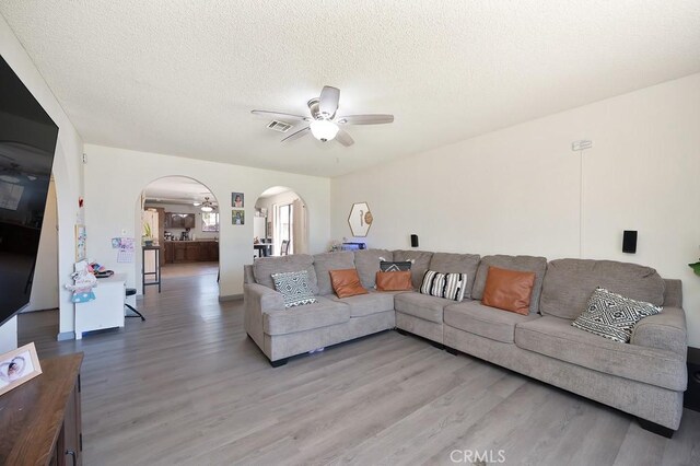1107 B St, Brawley, CA 92227 - living room featuring a ceiling fan, a textured ceiling, visible vents, arched walkways, and light wood finished floors
