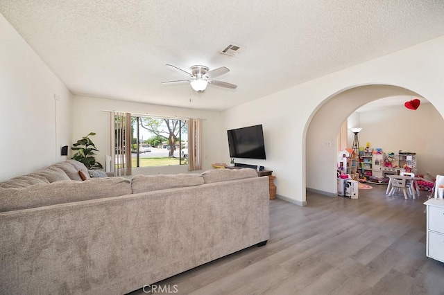 1107 B St, Brawley, CA 92227 - living room featuring ceiling fan, a textured ceiling, visible vents, arched walkways, and light wood-style flooring