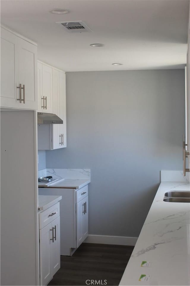 kitchen featuring visible vents, baseboards, under cabinet range hood, white cabinetry, and dark wood-type flooring