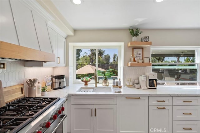 kitchen featuring custom exhaust hood, stainless steel stove, a sink, backsplash, and white cabinets