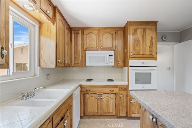 kitchen with a sink, white appliances, tile counters, brown cabinetry, and decorative backsplash