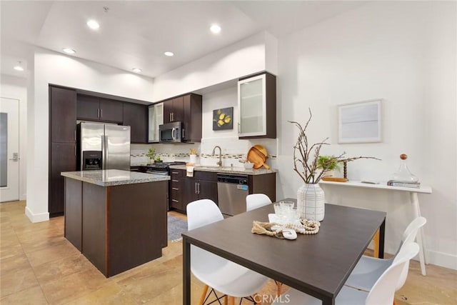 kitchen featuring dark brown cabinetry, appliances with stainless steel finishes, a sink, backsplash, and a kitchen island