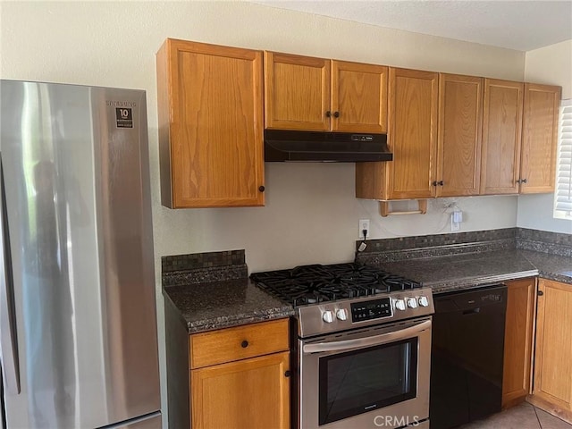 kitchen featuring appliances with stainless steel finishes, brown cabinets, under cabinet range hood, and dark stone countertops
