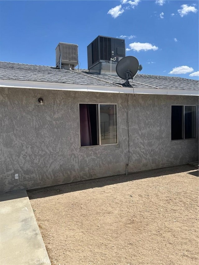 view of side of property featuring central AC and roof with shingles