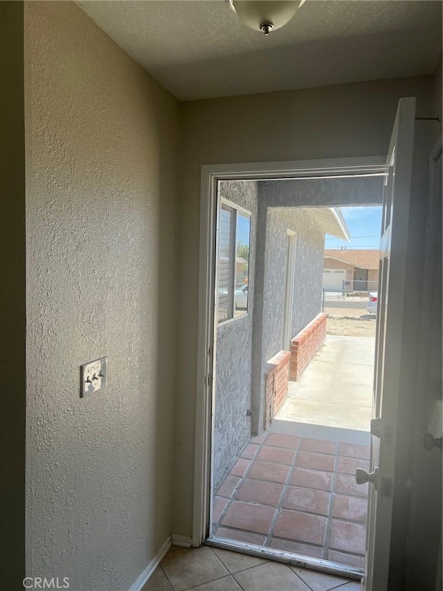 doorway featuring baseboards, a textured wall, and tile patterned floors