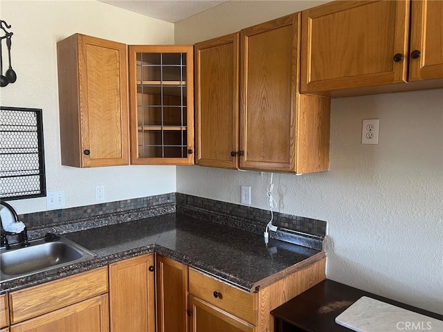 kitchen with brown cabinetry, a sink, a textured wall, and glass insert cabinets