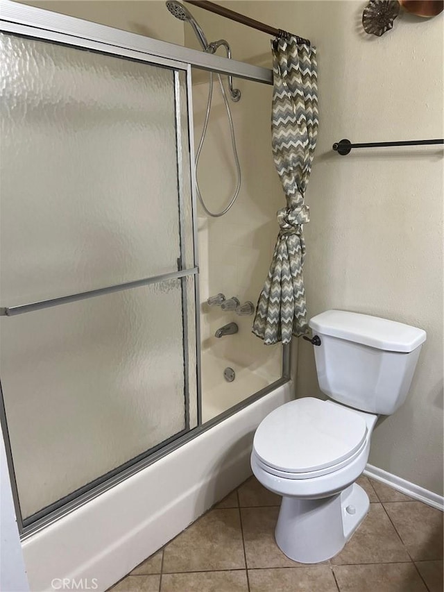 bathroom featuring baseboards, shower / bath combination with glass door, tile patterned floors, and toilet