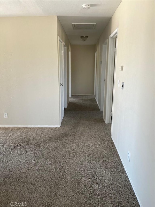 hall featuring baseboards, attic access, and carpet