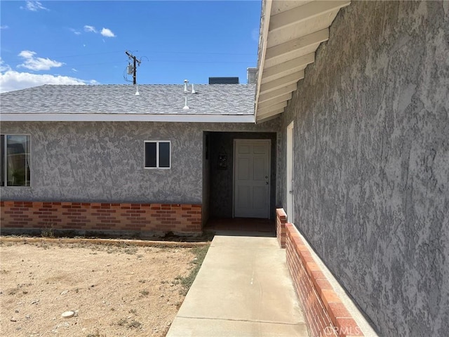 view of exterior entry featuring brick siding and stucco siding