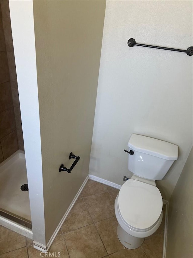 bathroom with toilet, tile patterned floors, baseboards, and a stall shower