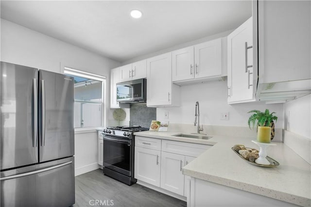kitchen featuring a sink, stainless steel appliances, light wood-type flooring, and white cabinetry