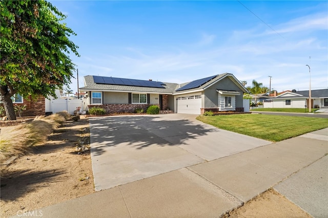 view of front of property with fence, a front yard, roof mounted solar panels, concrete driveway, and an attached garage