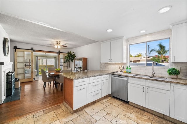 kitchen featuring backsplash, stainless steel dishwasher, a barn door, a sink, and a peninsula