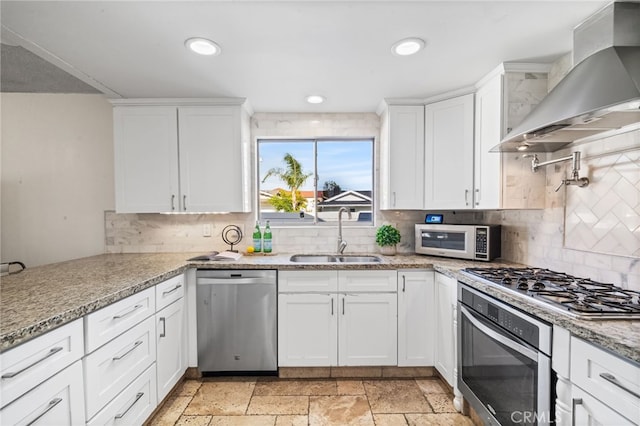 kitchen featuring wall chimney exhaust hood, white cabinetry, a sink, backsplash, and stainless steel appliances