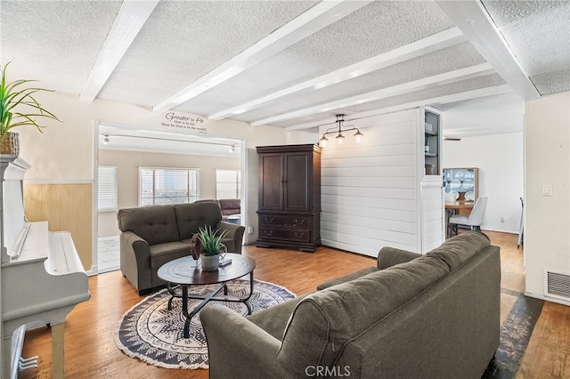 living room featuring a textured ceiling, wood walls, beam ceiling, and wood finished floors