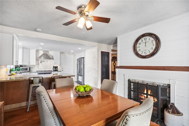 dining space with a textured ceiling, ceiling fan, dark wood finished floors, and a glass covered fireplace