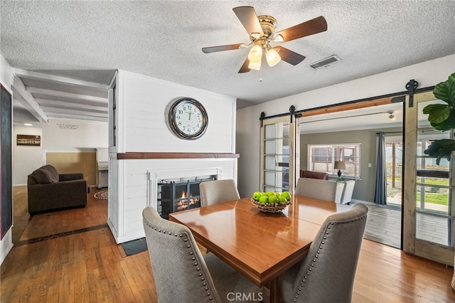 dining room with a warm lit fireplace, visible vents, a barn door, and wood finished floors