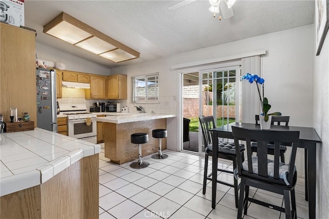 9684 Hemlock St, Rancho Cucamonga, CA 91730 - kitchen featuring white gas stove, tile counters, freestanding refrigerator, under cabinet range hood, and a peninsula
