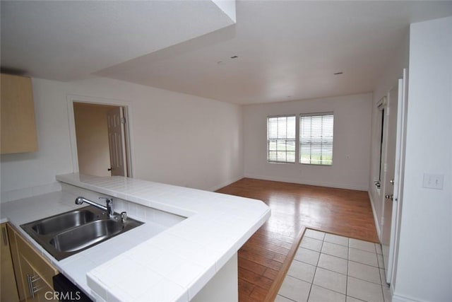 kitchen with tile countertops, a sink, a peninsula, open floor plan, and light wood-style flooring