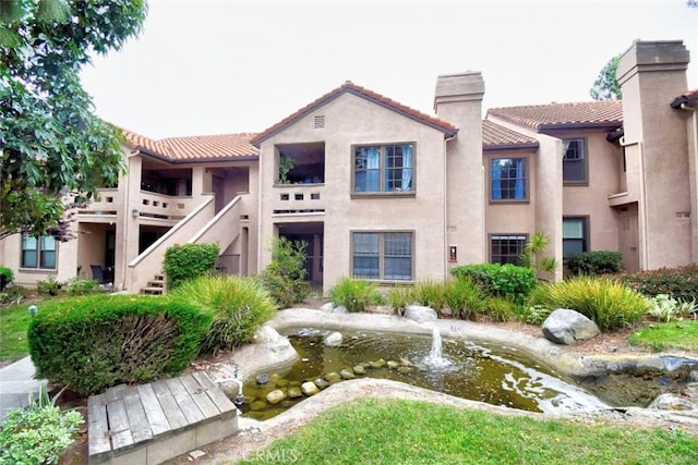 view of front of house featuring a garden pond, a chimney, a tile roof, and stucco siding