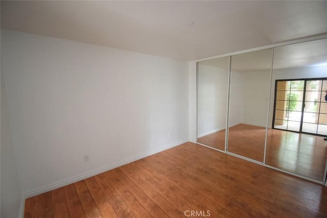 unfurnished bedroom with baseboards, hardwood / wood-style flooring, and a closet