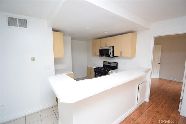kitchen featuring light brown cabinetry, stainless steel appliances, baseboards, a peninsula, and visible vents