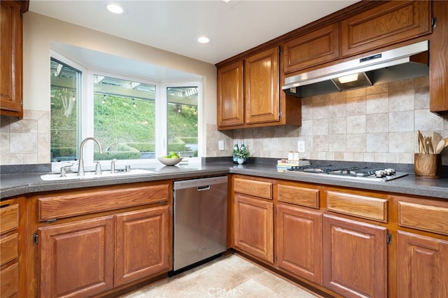 kitchen featuring brown cabinets, dark countertops, appliances with stainless steel finishes, a sink, and under cabinet range hood
