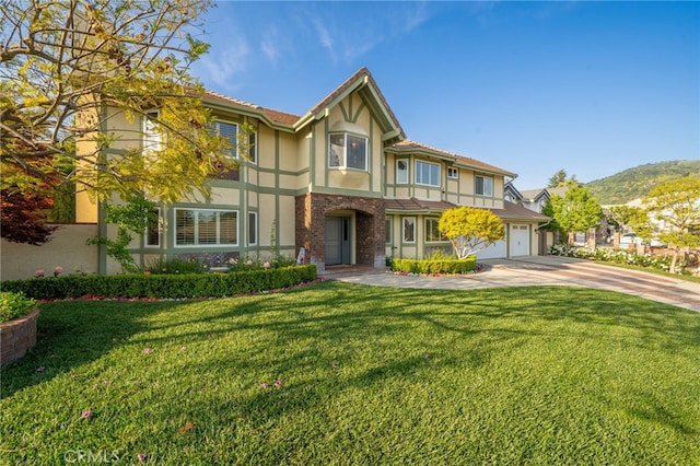 tudor house with driveway, a garage, a mountain view, a front lawn, and stucco siding