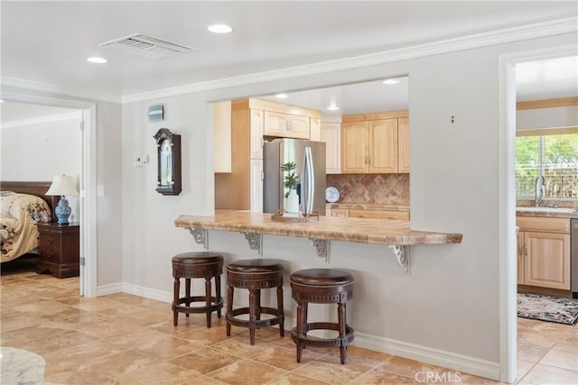 kitchen with visible vents, light brown cabinetry, a breakfast bar, baseboards, and appliances with stainless steel finishes