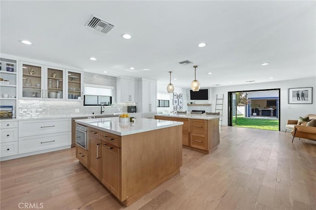kitchen featuring glass insert cabinets, open floor plan, visible vents, a kitchen island, and tasteful backsplash