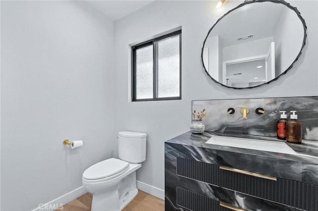 half bath featuring toilet, wood finished floors, visible vents, baseboards, and tasteful backsplash
