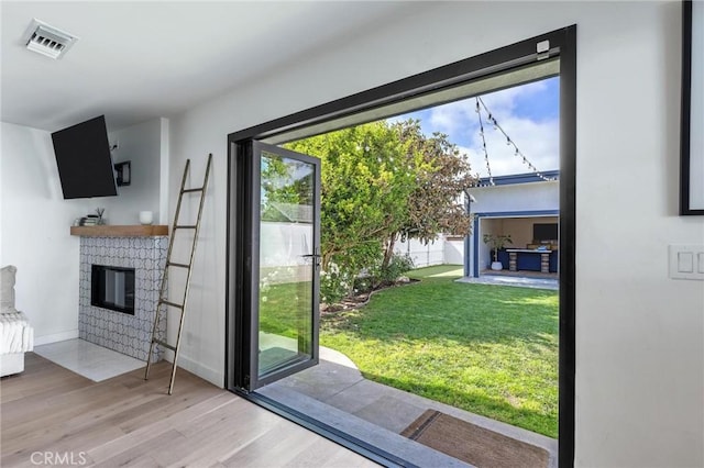 doorway with a brick fireplace, baseboards, visible vents, and wood finished floors
